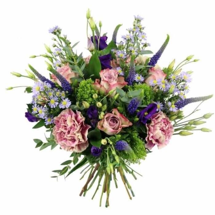 This photograph features a voluminous, dome-shaped bouquet positioned against a bright white background, its palette of pink, mauve, and purple blooms set off beautifully by lively greens, evoking the relaxed charm of Old Malden's leafy avenues. In the centre, several soft pastel pink roses take pride of place, their petals unfolding in elegant spirals from deeper, rosy cores to lighter, almost blush-cream edges. Some of the roses are more tightly furled, hinting at freshness, while others open more generously, adding a sense of maturity and fullness. Tucked closely among them are large, ruffled carnations in tones of dusty rose and purple-mauve, each bloom formed of many overlapping petals that create a frilly, almost cloud-like texture. Threaded through this softness, tall spires of deep lavender-blue Veronica stand upright, adding height and a subtle sense of movement, as though caught in a gentle breeze. Nestled alongside, rich purple lisianthus blossoms introduce deeper, jewel-like notes to the composition, their bell-shaped flowers lending a soft, velvety sheen that plays beautifully against the more matte petals of the carnations. Light, airy sprays of aster-style flowers in pale lavender-blue, each with a tiny yellow centre, weave between the larger blooms, filling gaps and adding a fine, starry delicacy. Surrounding and supporting the flowers is a mix of greenery: vibrant, chartreuse-coloured filler that brings an energetic brightness, teamed with cool, silvery eucalyptus leaves and other soft green foliage that arc around the bouquet and give it structure. From a slightly overhead perspective, the neatly bundled stems can be seen at the base, bound tightly to form a traditional hand-tied arrangement, ready for a favourite vase on a kitchen table or sideboard. The overall feeling is one of quiet sophistication and heartfelt warmth, perfect for marking birthdays, anniversaries, or thoughtful gestures in homes across Old Malden and the local area, and crafted with the care you'd expect from Florist Old Malden.